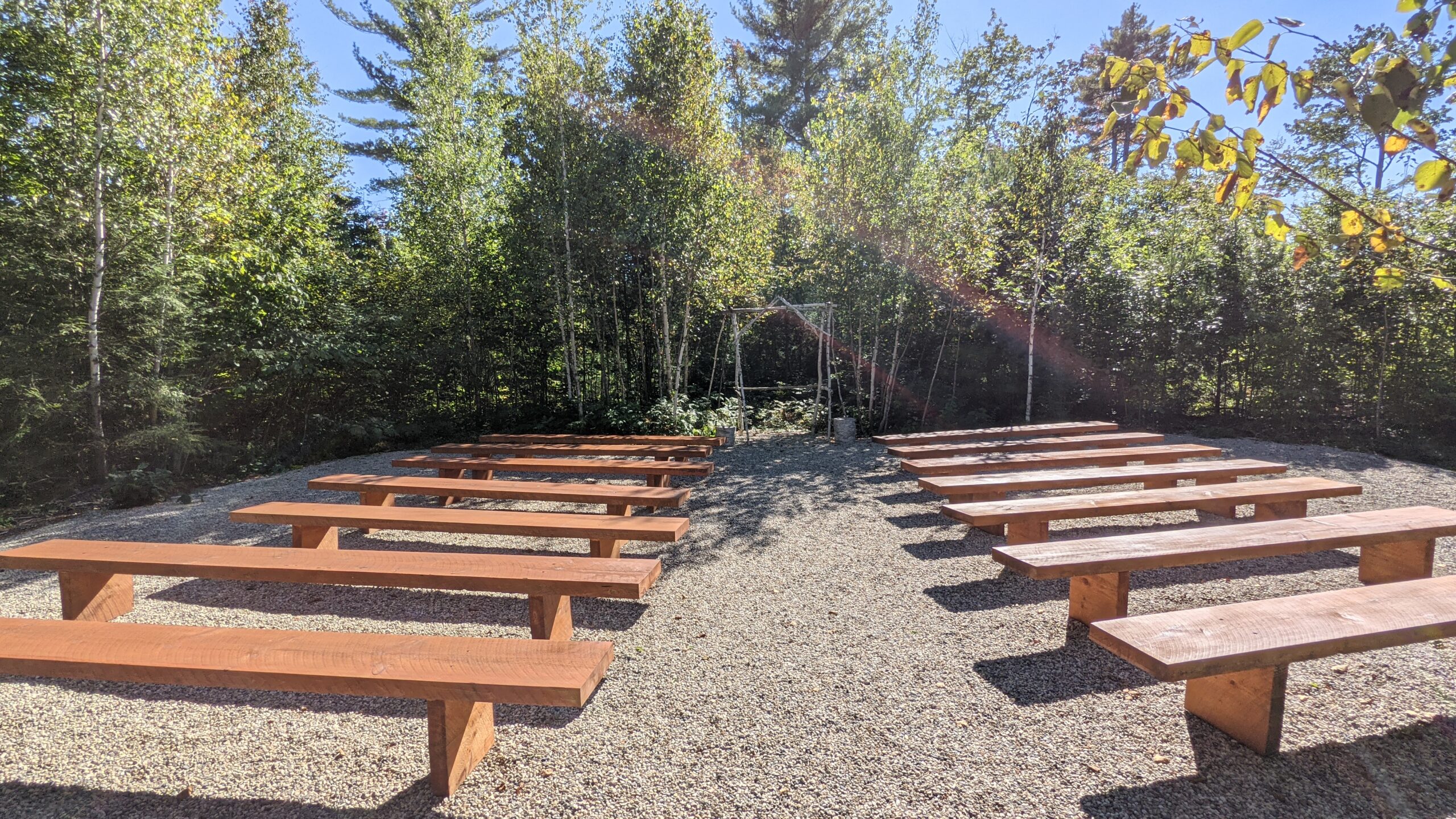 Wooded ceremony area with slab benches and mini birch arbor